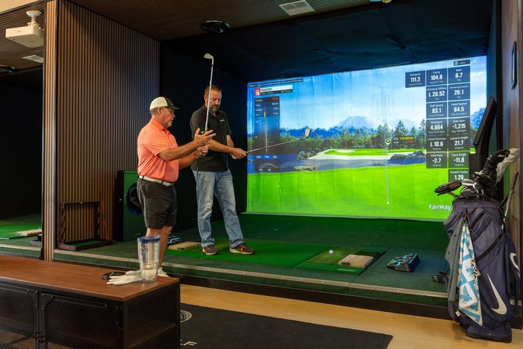 Eric Brasch coaching in a simulator bay, adjusting a golfer&rsquo;s grip