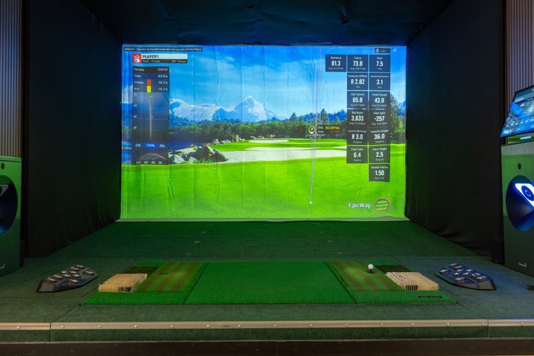 An empty hitting bay, the GOLFZON screen showing a course and a full shot-data panel