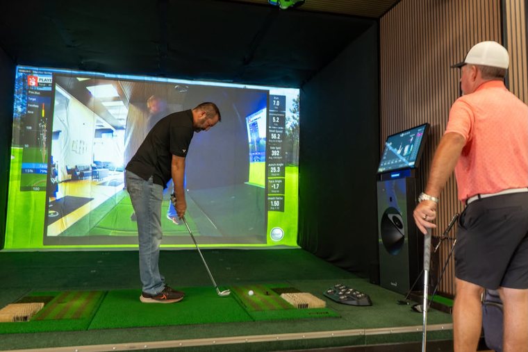 A golfer at address in a bay, with swing video replayed on the screen