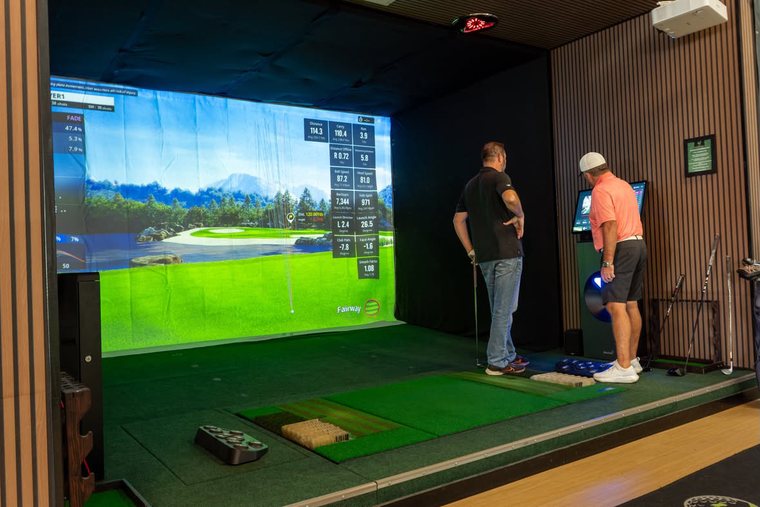 Two golfers in a bay reading the shot data after a swing