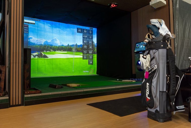A simulator bay seen past a golf bag on the studio floor