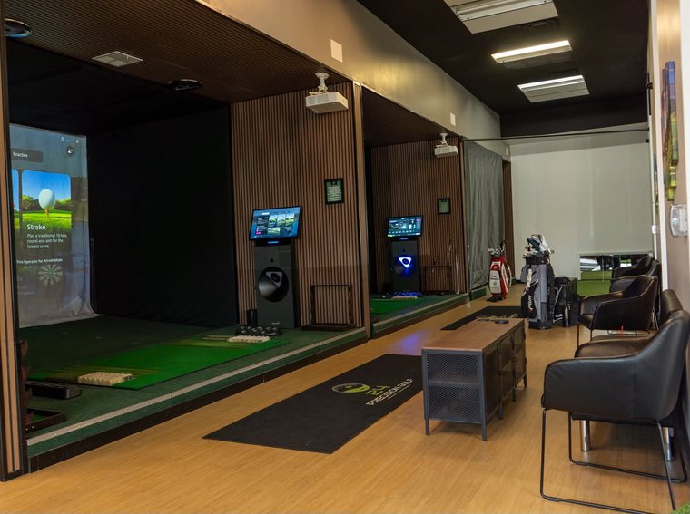 Two simulator bays with lounge chairs and the 24 Precision Golf floor mat