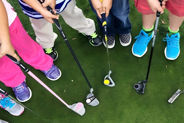 Junior golfers standing over their putters on the practice green