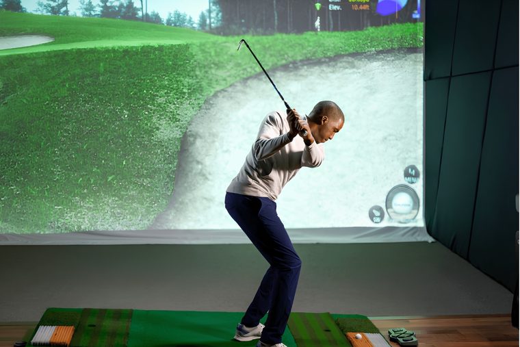 A golfer at the top of the backswing in a simulator bay, shot data on screen
